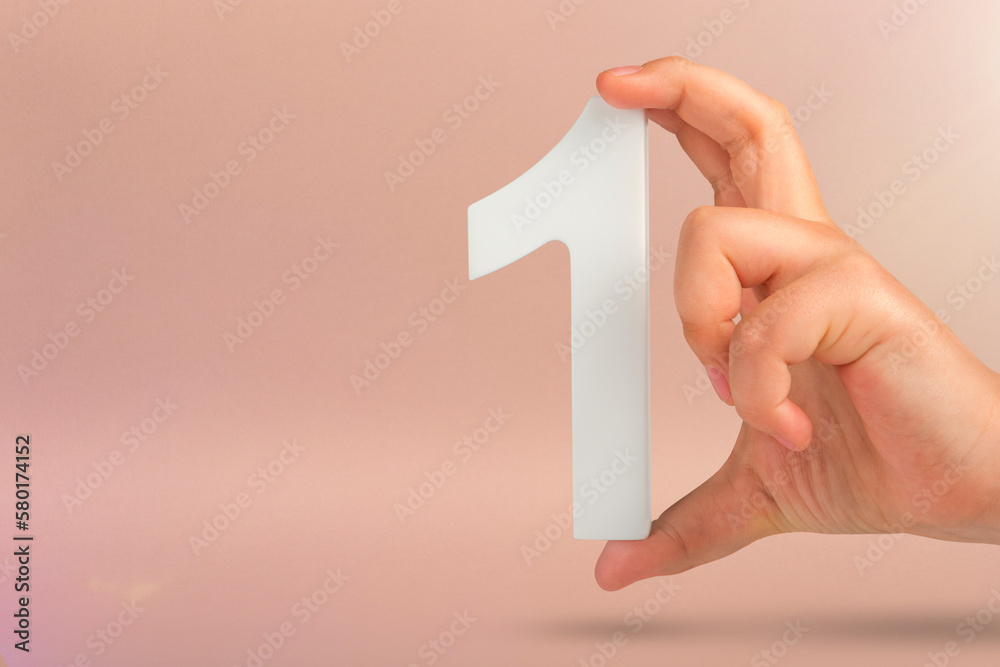 Aufkleber Number one in hand. A hand holds a white number one on a red background with copy space. Concept with number one. 1 percent rate, birthday, first or winner.