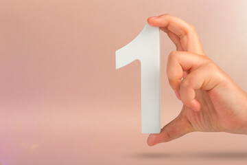 Number one in hand. A hand holds a white number one on a red background with copy space. Concept with number one. 1 percent rate, birthday, first or winner.
