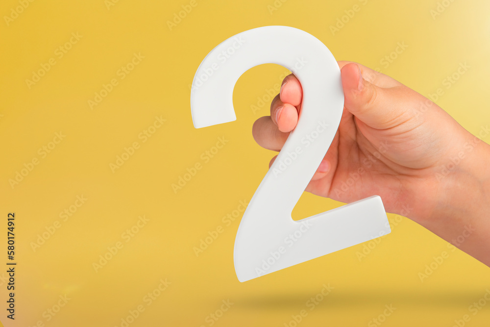Aufkleber number two in hand. hand holding white number 2 on yellow background with copy space. concept with n