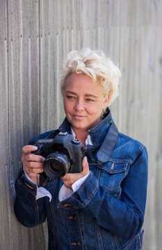 Portrait of attractive mature blond woman outdoors taking pictures with DSLR camera.