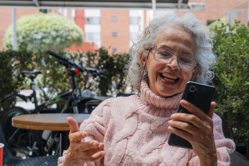 Joyful Senior woman Connects Virtually in Sunny Outdoor Cafe