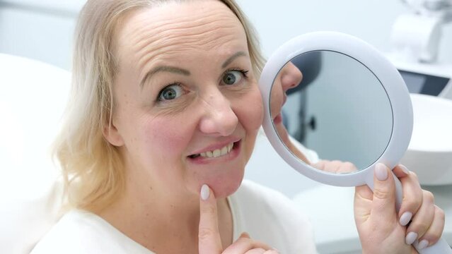 beautiful young middle-aged woman admiring herself in mirror in dental chair after whitening procedure cleaning teeth filling pleased winks at frame and laughs camera is approaching slow motion