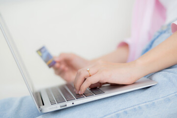 Fototapeta na wymiar Closeup hands of woman sitting on sofa using laptop computer online shopping with credit card, happy female payment with debit card on couch, purchase and payment, business and technology concept.