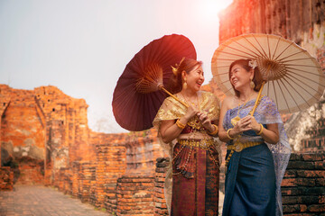 happiness face of two asian woman wearing old thai traditional suit with bamboo umbrella standing in old temple  at ayutthaya world heritage site of unesco thailand