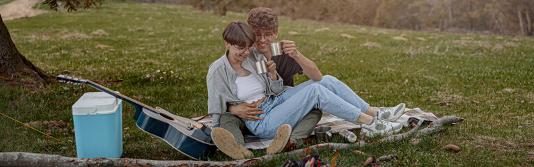 Happy young couple of tourists sitting in hug and laughing while having picnic. Weekend.