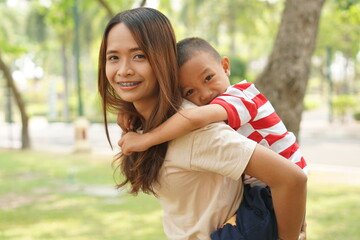A boy happily rides on his mother's back in the park.