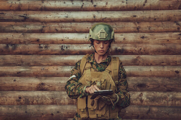 Woman soldier using tablet computer against old wooden wall in camp