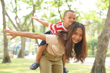 A boy happily rides on his mother's back in the park.