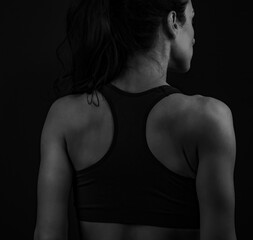 Naklejka premium Female sporty muscular with ponytail doing stretching workout the shoulders, blades and arms in sport bra, standing on dark shadow grey background with empty copy space. Back view.