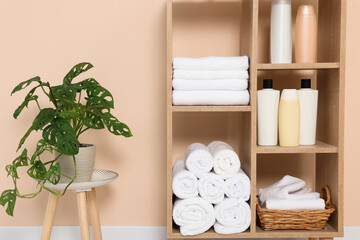 Soft folded towels and cosmetic bottles on wooden shelving unit near beige wall