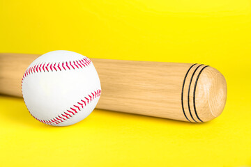 Wooden baseball bat and ball on yellow background, closeup. Sports equipment