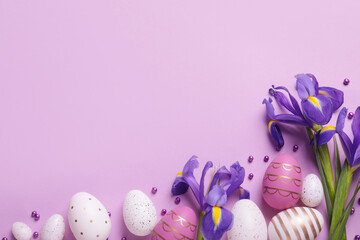 Flat lay composition with festively decorated Easter eggs and iris flowers on violet background....
