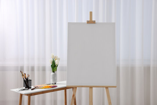 Wooden easel with canvas and art supplies on table indoors. Space for text