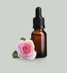 Bottle of rose essential oil and flower on light background