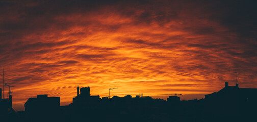 Panoramic view of a bright orange sunset, contrasting the silhouettes of the city's buildings and...