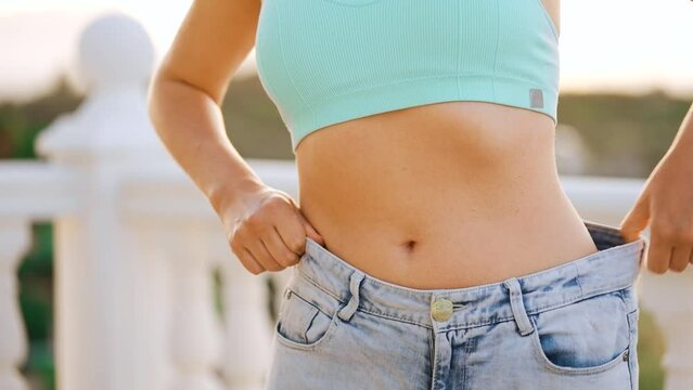 Woman enjoy weight loss at home. Female in old jeans after successful diet. 