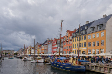 Fototapeta premium Aerial view of Nyhavn canal with floating tour boat which full of tourists and background of colourful iconic townhouses along waterfront during cloudy day.