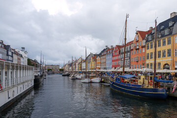 Fototapeta premium Aerial view of Nyhavn canal with floating tour boat which full of tourists and background of colourful iconic townhouses along waterfront during cloudy day.