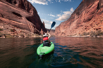 Fototapeta Adventurous Woman on a Kayak paddling in Colorado River. Glen Canyon, Arizona, United States of America. American Mountain Cloudy Sky Art Render. Adventure Travel obraz