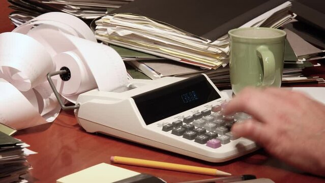 Time lapse of a man's hand using a calculator on a cluttered office desk.