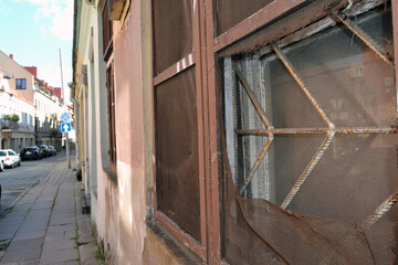 Selective focus of perspective view of narrow city street along wall of old house with focus on broken window