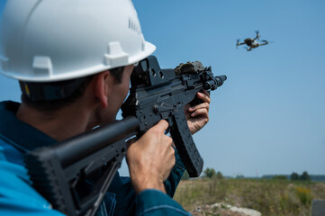 Caucasian man in a helmet shoots a flying drone with a rifle. 