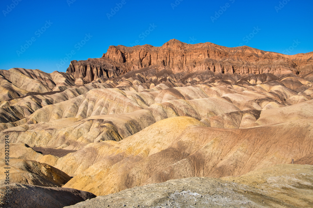 Wall mural wide view of remote desert mountains and rolling hills with colorful layers of rock on a clear day.