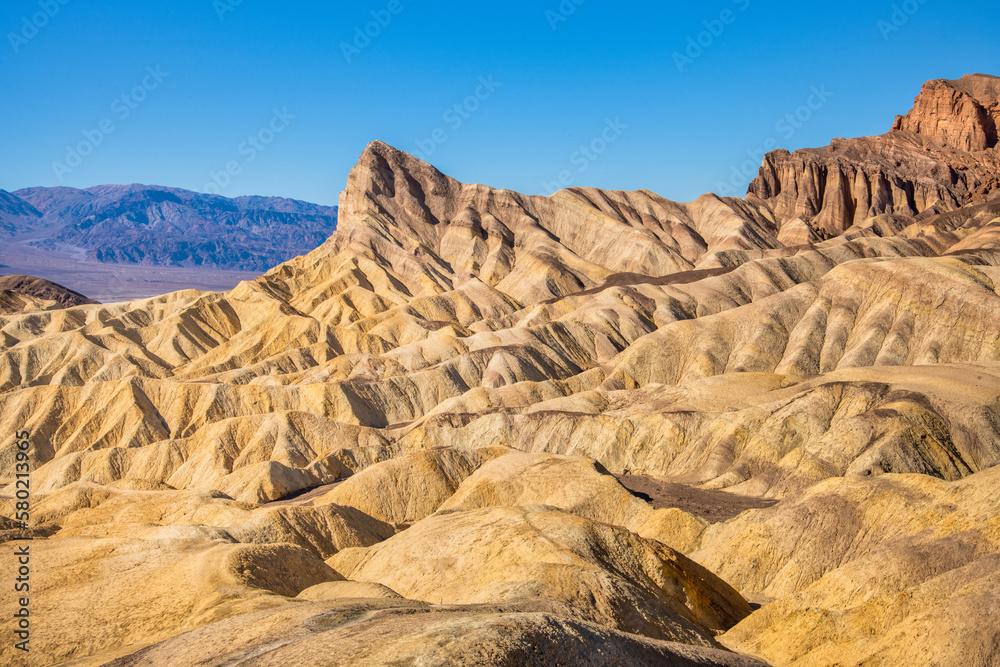 Wall mural wide view of remote desert mountains and rolling hills with colorful layers of rock on a clear day.