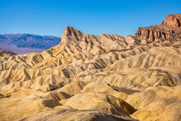 Wide view of remote desert mountains and rolling hills with colorful layers of rock on a clear day.
