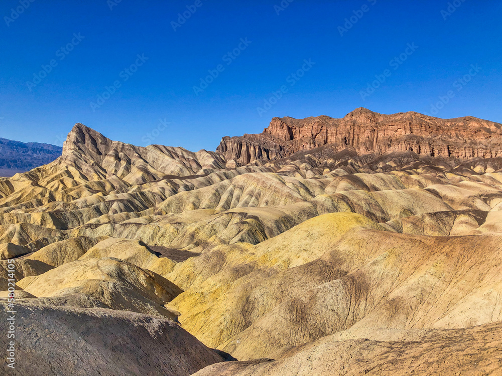 Wall mural wide view of remote desert mountains and rolling hills with colorful layers of rock on a clear day.
