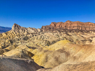 Wide view of remote desert mountains and rolling hills with colorful layers of rock on a clear day.