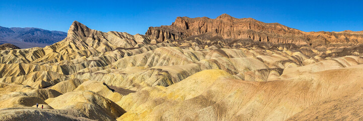 Panoramic view of remote desert mountains and rolling hills with colorful layers of rock on a clear day.