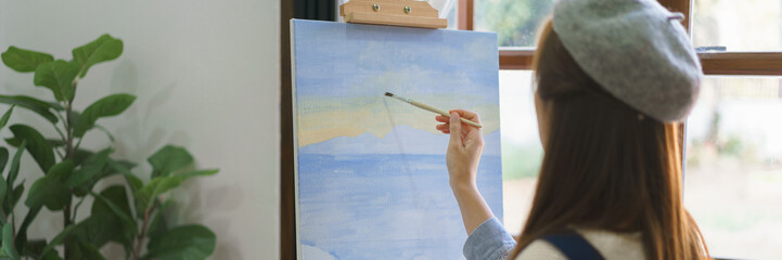 Young female painter using paintbrush to drawing and painting masterpiece on canvas in home studio