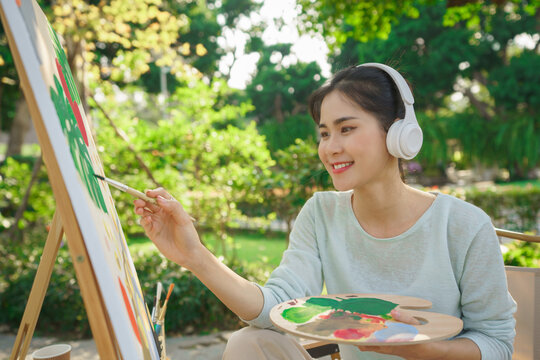 Outdoor activity concept, Female artist listening music while painting picture on canvas in garden
