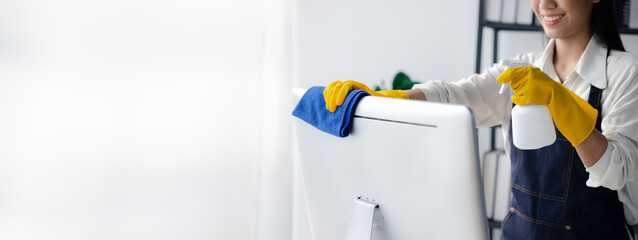 Person cleaning room, cleaning worker is using cloth to wipe computer screen in company office room. Cleaning staff. Concept of cleanliness in the organization.