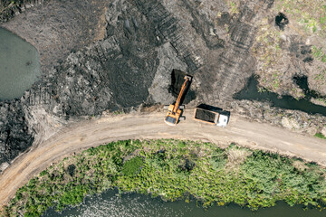 swamp area reclamation for building works. excavator loads soil into dump truck. aerial top view.