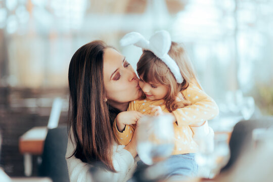 Mother Kissing her Child Wearing Bunny Ears on Easter. Happy mom and her daughter having fun bonding in a restaurant
