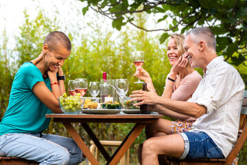 Group of friends laughing, talking and drinking wine during garden dinner party.