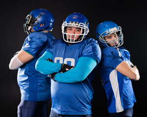 Portrait of three men in blue American football uniforms standing with their arms crossed over their chests on a black background. 