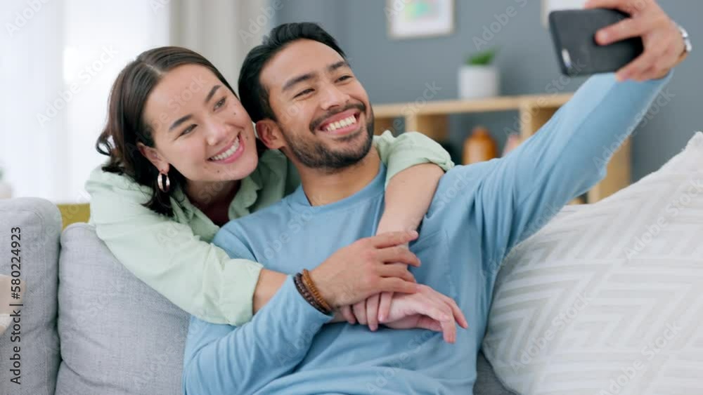 Poster Asian couple taking selfie on phone at home, love and care for social media post and smile for camera in living room at home. Man and woman giving hug for picture on smartphone for internet app