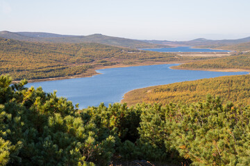 Autumn landscape. View from the hill to the reservoir on the river in a mountain valley. In the foreground, thickets of Siberian dwarf pine. Magadan region, Siberia, Far East of Russia.