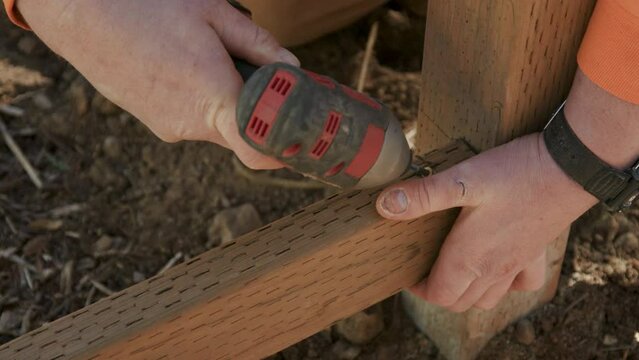 Close Up on Hands of Construction Worker Screwing in Fence Stringer to Post with Power Tool