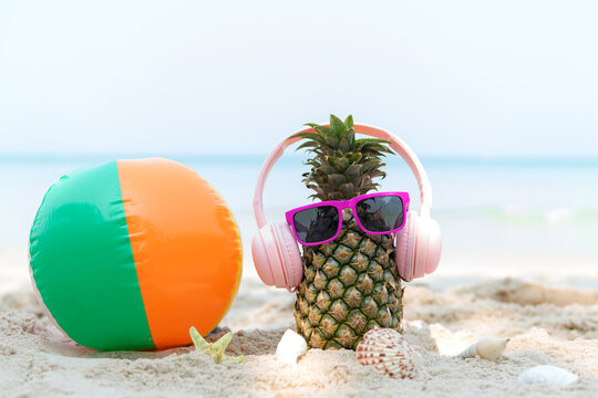 Summer in the party.  Hipster Pineapple Fashion in sunglass and listen music with ball beach on the sand beautiful blue sky background.  Creative art fruit for tropical style