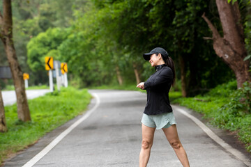 Fototapeta na wymiar Healthy woman warming up stretching her arms. Asian runner woman workout before fitness and jogging session on the road nature park. Healthy and Lifestyle Concept