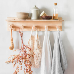 Linen towels on a wooden shelf with bowls,  ceramic jar, brushes, dried flowers in a  cozy kitchen in a scandinavian style