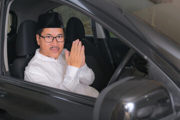 A middle-aged man positions his hands in front of his chest to say thank you before driving away; friendly expression.