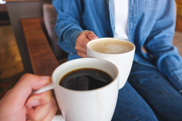 Closeup image of a couple people clinking white coffee mugs in cafe