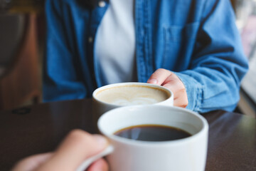Closeup image of a couple people clinking white coffee mugs in cafe - obrazy, fototapety, plakaty