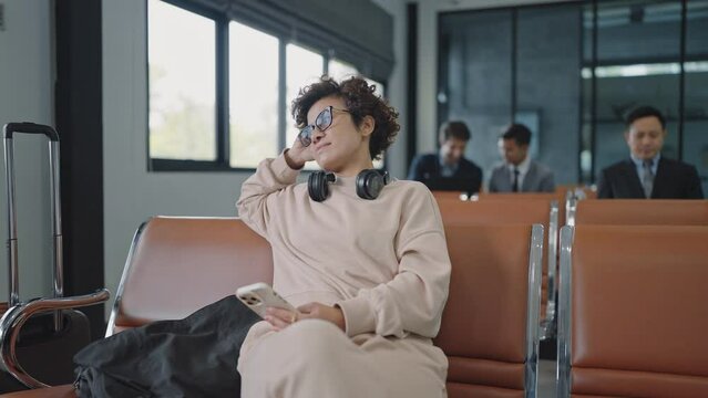 Asian woman tourists sitting and waiting for flight at airport terminal holding smartphone and headphone