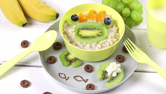 Funny bowl of oatmeal with frog faces made from fruits and berries. Food idea for kids, top view